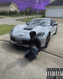 a man kneeling in front of a car with a parental advisory sticker