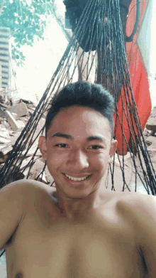 a shirtless young man smiles for the camera while laying in a hammock