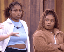 two women standing next to each other with their arms crossed and one is wearing a blue crop top