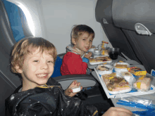 two young boys are sitting at a table with a tray of food on it