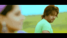 a man and a woman are standing in a field . the man is wearing a green shirt .