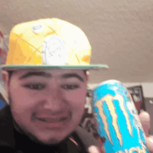 a man wearing a yellow hat is holding a monster energy drink