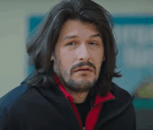 a man with long hair and a beard is wearing a red jacket