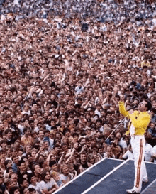 a man in a yellow jacket is singing into a microphone in front of a crowd of people .