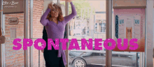 a woman in a purple dress is dancing in front of a sign that says spontaneous on it