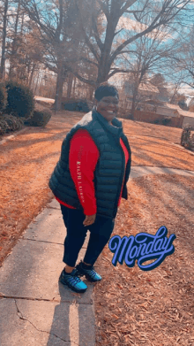 a woman wearing a red shirt and a black vest is standing on a sidewalk on monday