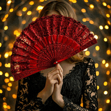 a woman in a black lace dress is holding a red fan in front of her face