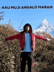 a man in a red jacket stands in front of a mountain with the words " aau muji angalo maram " written above him