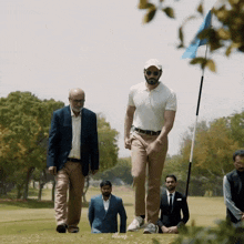 a group of men are walking on a golf course with a blue flag in the background that says allwaj