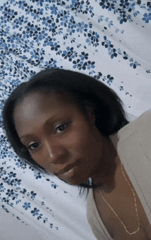 a woman laying on a bed with a blue and white floral curtain in the background