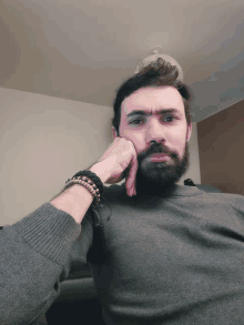 a man with a beard wearing a gray sweater has his hand on his face