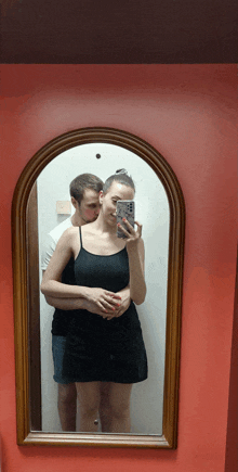 a man kisses a woman on the cheek while she takes a picture of herself in a mirror