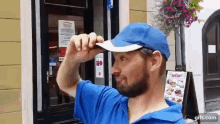 a man wearing a blue shirt and a white hat is standing in front of a restaurant holding a menu .