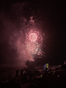 a crowd of people watching a fireworks display with neon glow sticks in the foreground