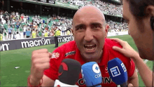 a man in a red shirt with the word macron on it is talking into a microphone