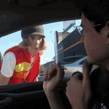 a woman in a red vest is talking to a man in a car in front of a sign that says united supplies