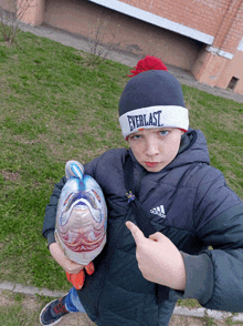 a boy wearing a everlast hat holds a fish balloon