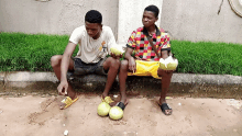 two young men are sitting on the sidewalk eating fruit