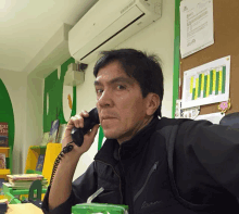 a man talking on a phone in front of a bulletin board