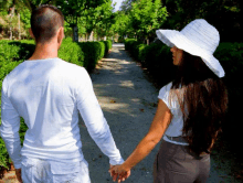 a man and a woman are holding hands while walking down a path