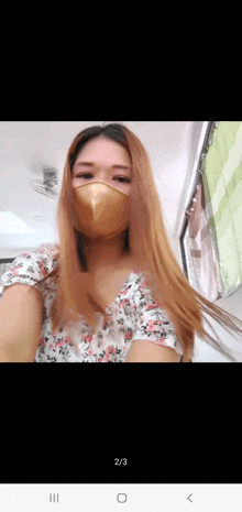 a woman wearing a mask and a floral top is taking a selfie