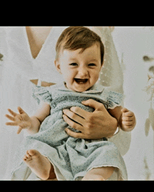 a baby in a blue dress is being held by a woman and smiling