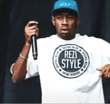 a man wearing a white t-shirt that says rez style is holding a microphone