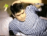 a man in a striped shirt is laying on a bed with his hands in his hair .