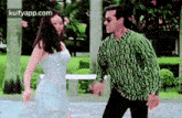 a man and a woman are dancing in a park . the woman is wearing a white dress .