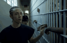 a woman in a black shirt is standing in a hallway next to a jail cell