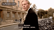 a man in a suit and tie is walking down a street with a pile of bicycles in the background ..