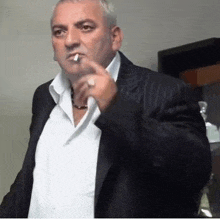 a man in a suit is smoking a cigarette while wearing a white shirt .