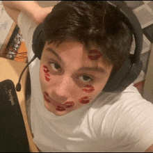 a man wearing headphones and a white shirt has red kisses on his face