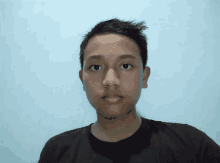 a young man in a black shirt looks at the camera with a blue background