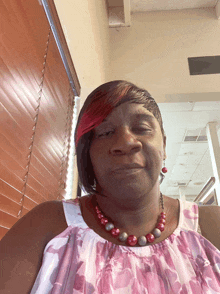 a woman wearing a pink and white floral shirt and a red necklace