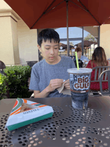 a boy sits at a table with a big gulp drink