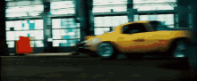 a yellow car is driving through a garage with a red box in the background