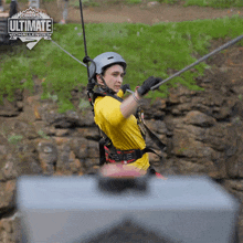 a man in a yellow shirt is hanging from a rope in front of a sign that says ultimate challenge