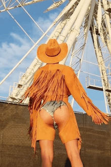 a woman in a cowboy outfit is standing in front of a large ferris wheel