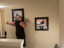 a woman in a black tank top is standing in front of two framed pictures on the wall