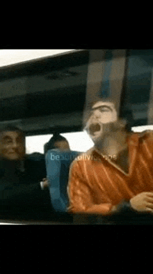 a man is yawning while sitting on a bus with other people .