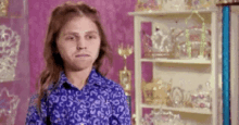 a young girl in a blue shirt is making a funny face in front of a shelf filled with trophies .