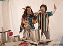 a man and a woman are standing next to each other in front of a table with paint cans .