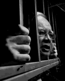 a black and white photo of a man behind bars .