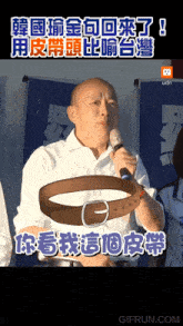 a man holding a microphone with a belt in front of him with chinese writing behind him