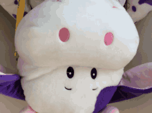 a white and purple stuffed animal with a pink embroidered face