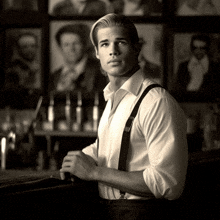 a man in a white shirt and suspenders leans on a bar counter