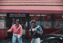 two men standing in front of a fast food restaurant with a sign that says " the best in town "