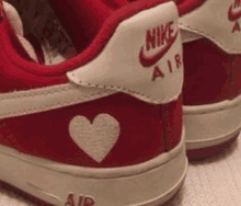 a pair of red and white nike air force 1 sneakers with a heart embroidered on the side .