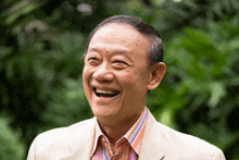 a man in a tan jacket and striped shirt laughs